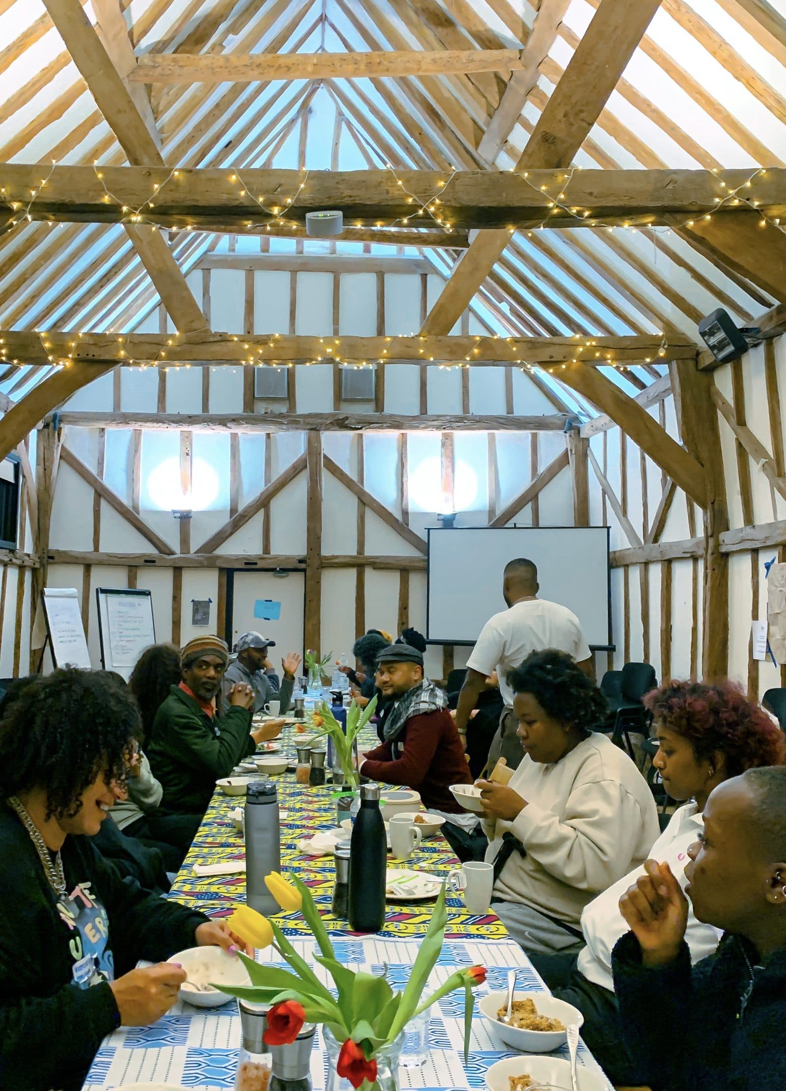 Retreat participants sharing a meal at a long table beneath fairy-lit barn rafters